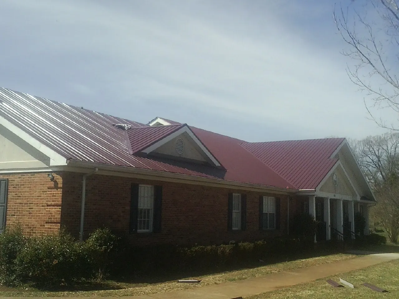 Red metal roof with gabled entries on a long brick building, from a Hail Damage Roof Repair job in New Galilee