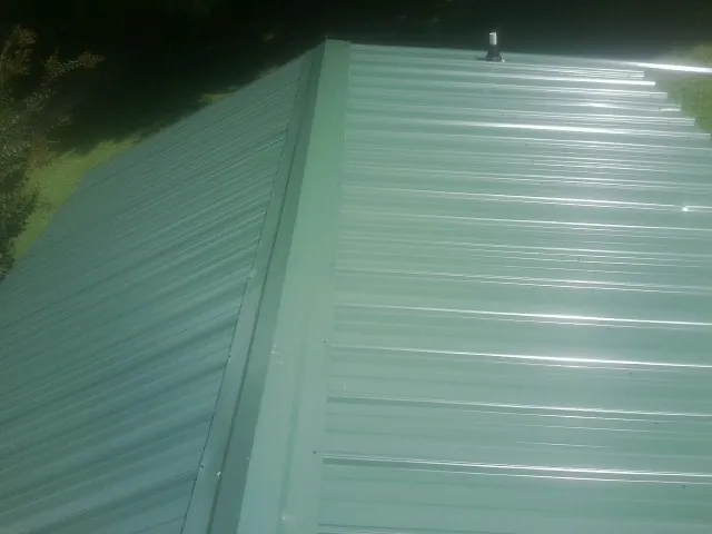 New green metal panels meeting at the ridge of a roof — Flat Roof Repair work by our crew in New Galilee