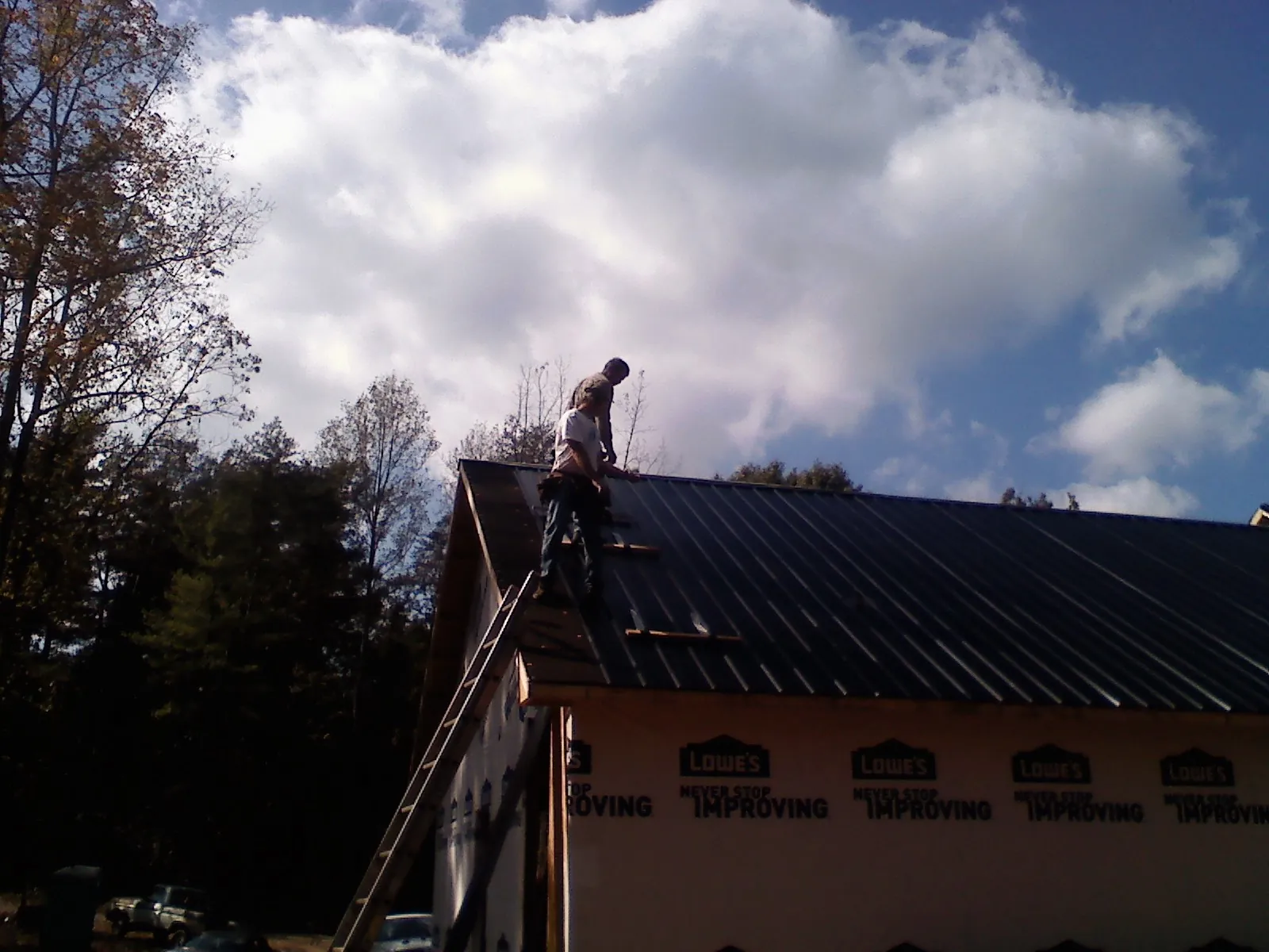 Roofer fastening dark metal panels high against a cloudy sky, from a Roof Inspection job in New Galilee