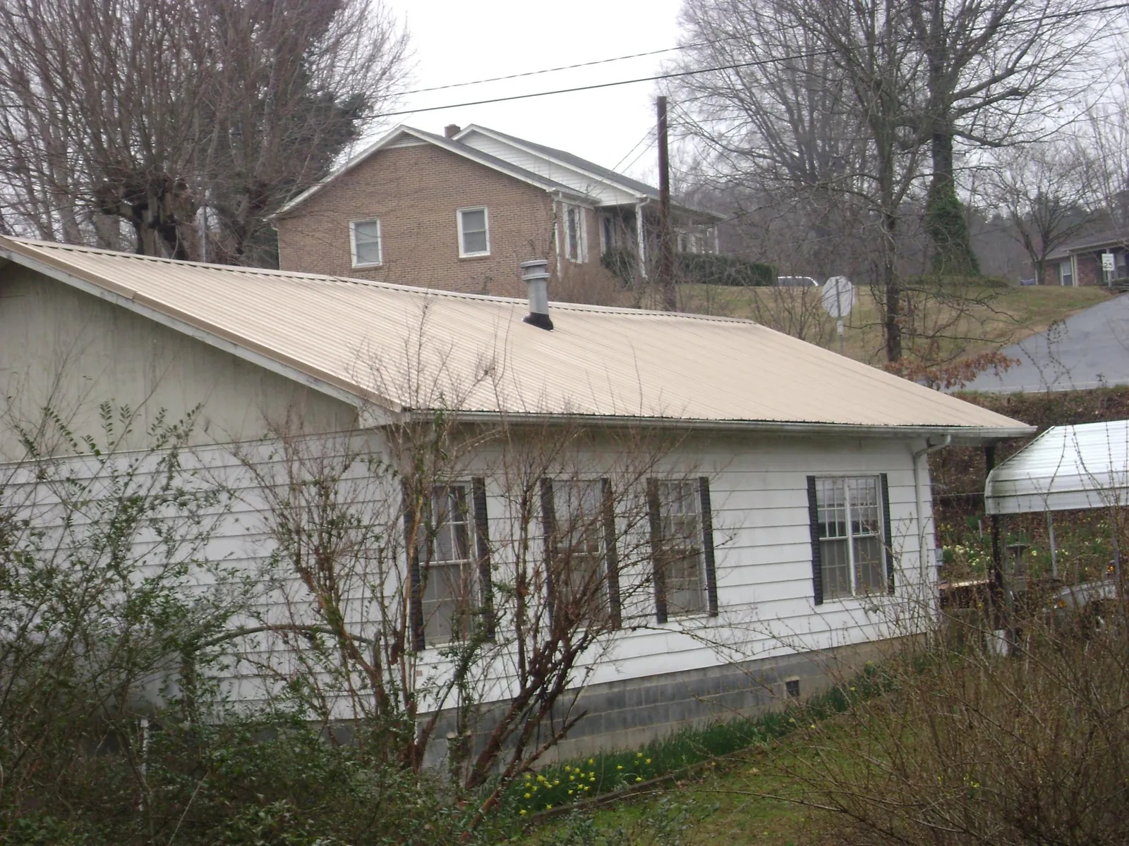 Tan metal roof on a white sided house set into a hillside — Commercial Roofing by Roofing Brothers in New Galilee